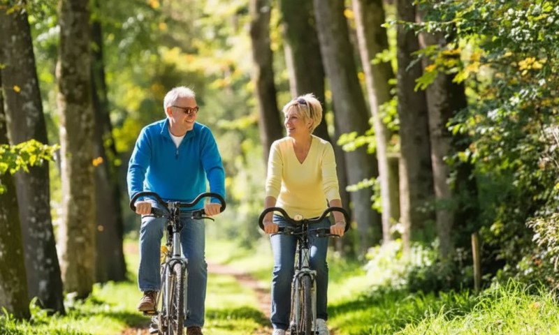 Stariji čovek i žena voze bicikle kroz šumu po sunčanom danu